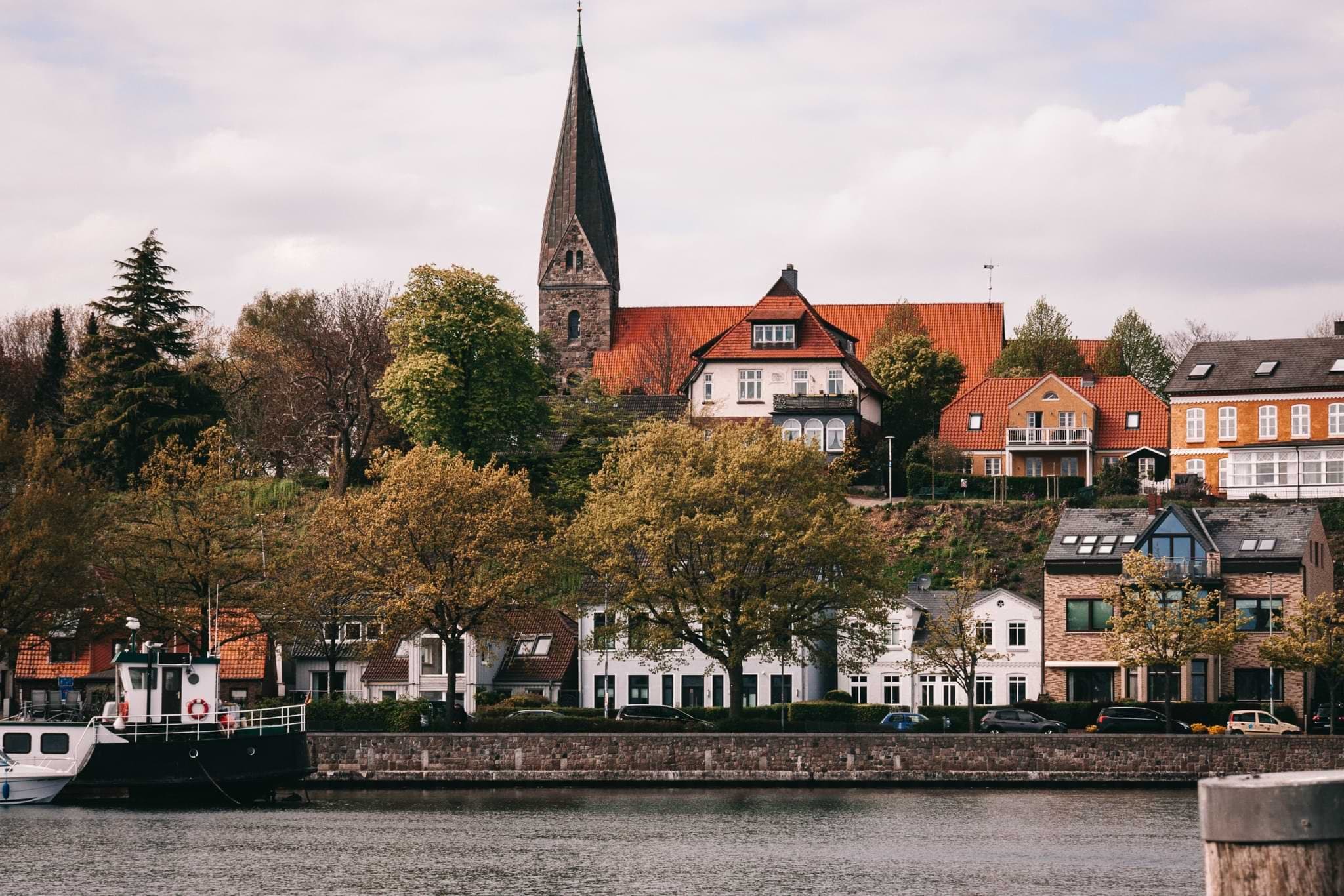 Colourful waterfront houses and a church spire above a moored boat in Eckernförde.