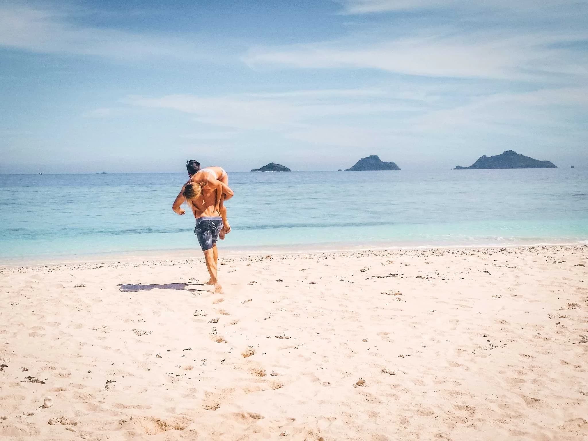 A person running towards clear turquoise water on Mana Island, Fiji, with small islands offshore.