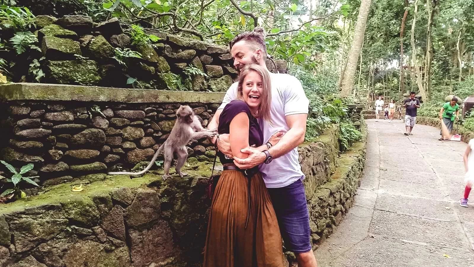 A couple beside a moss-covered wall in Ubud as a monkey reaches towards them.