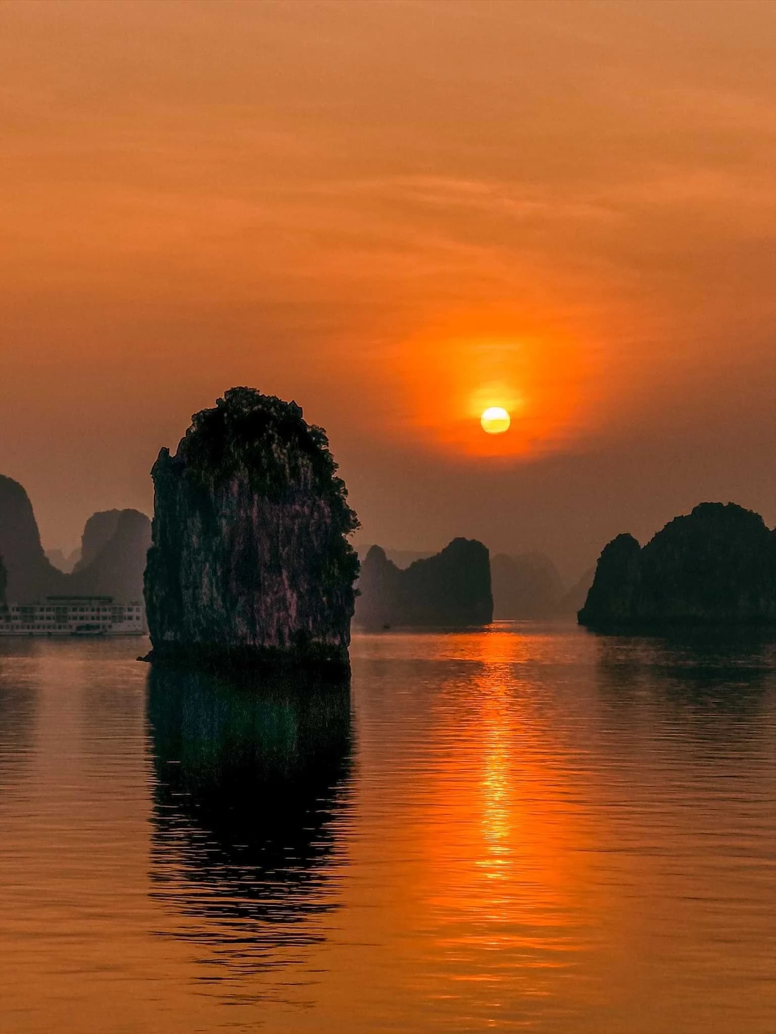 The orange sun above calm water and limestone islands in Ha Long Bay.