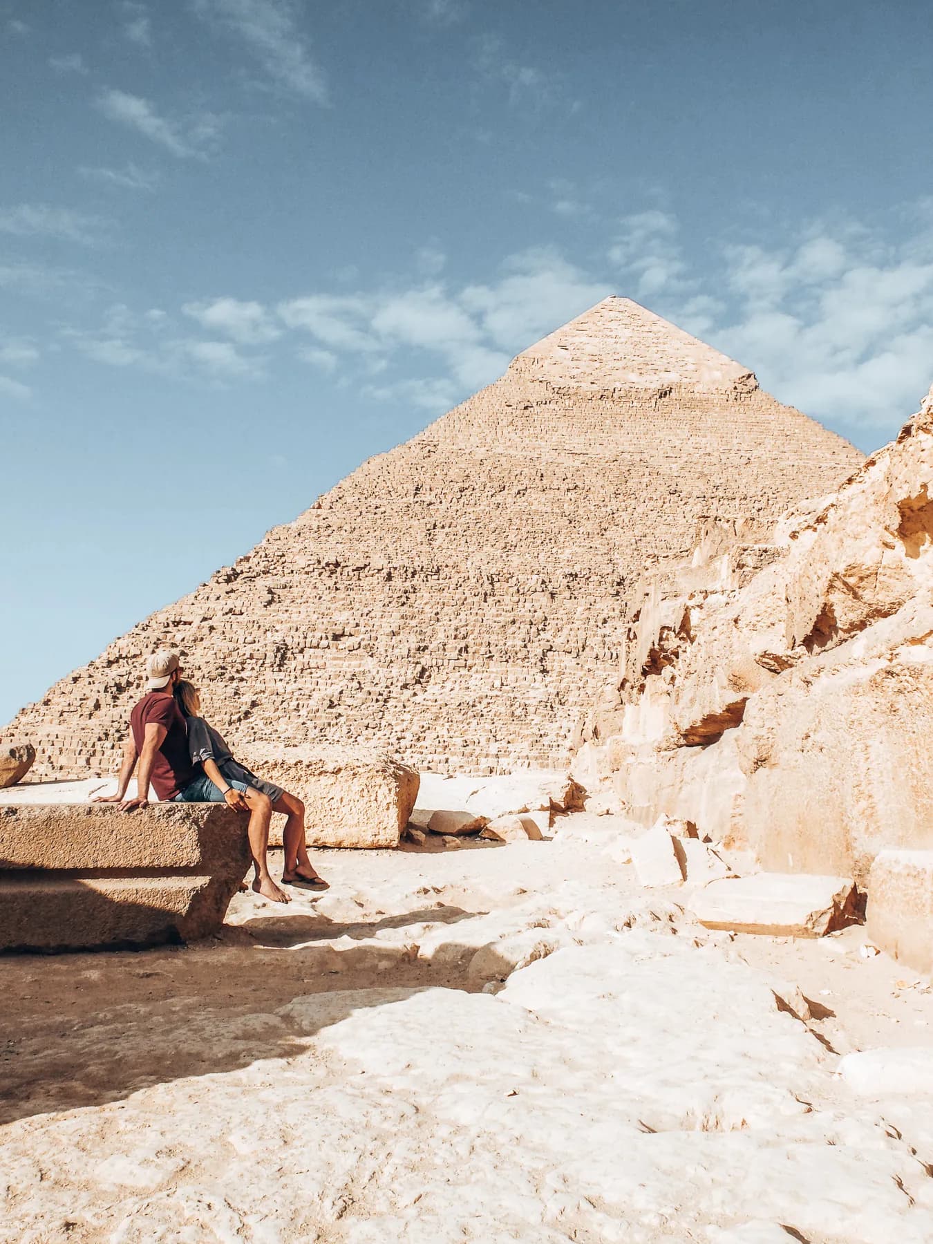 Two travellers sitting on stone blocks beside a pyramid.