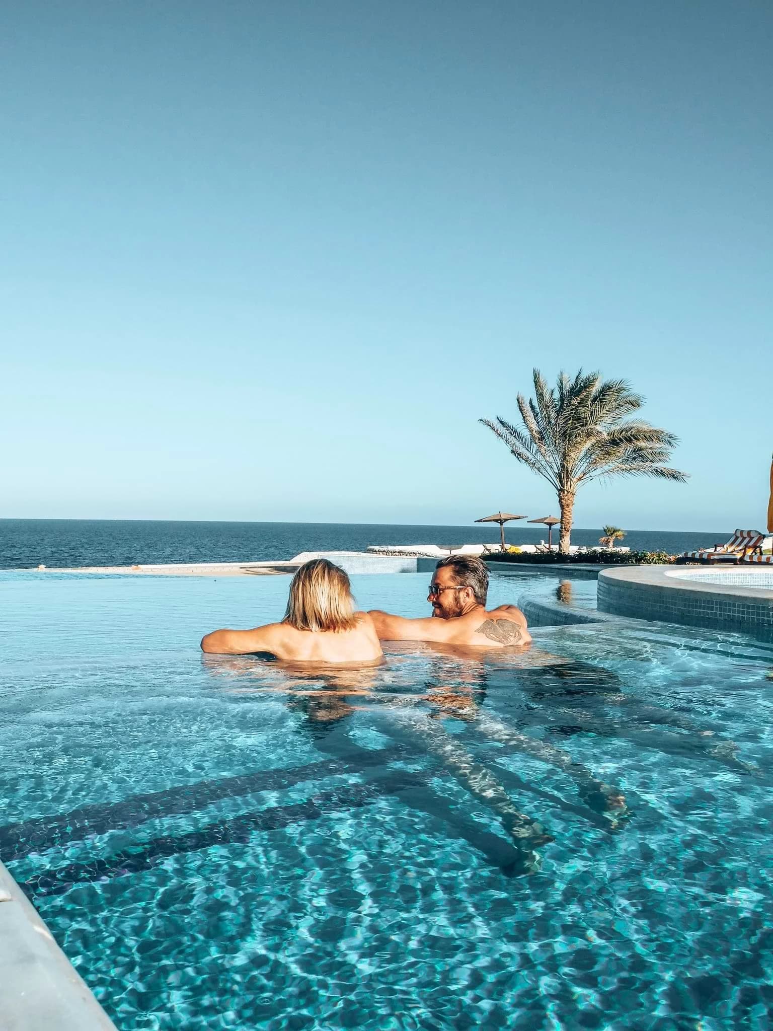 Two people relaxing in an infinity pool overlooking the sea.