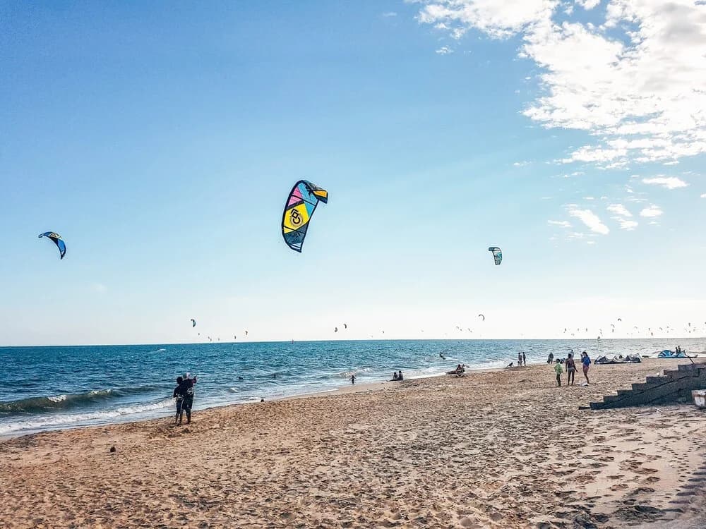 Kites flying above riders and beachgoers along the sandy shoreline at Mui Ne.