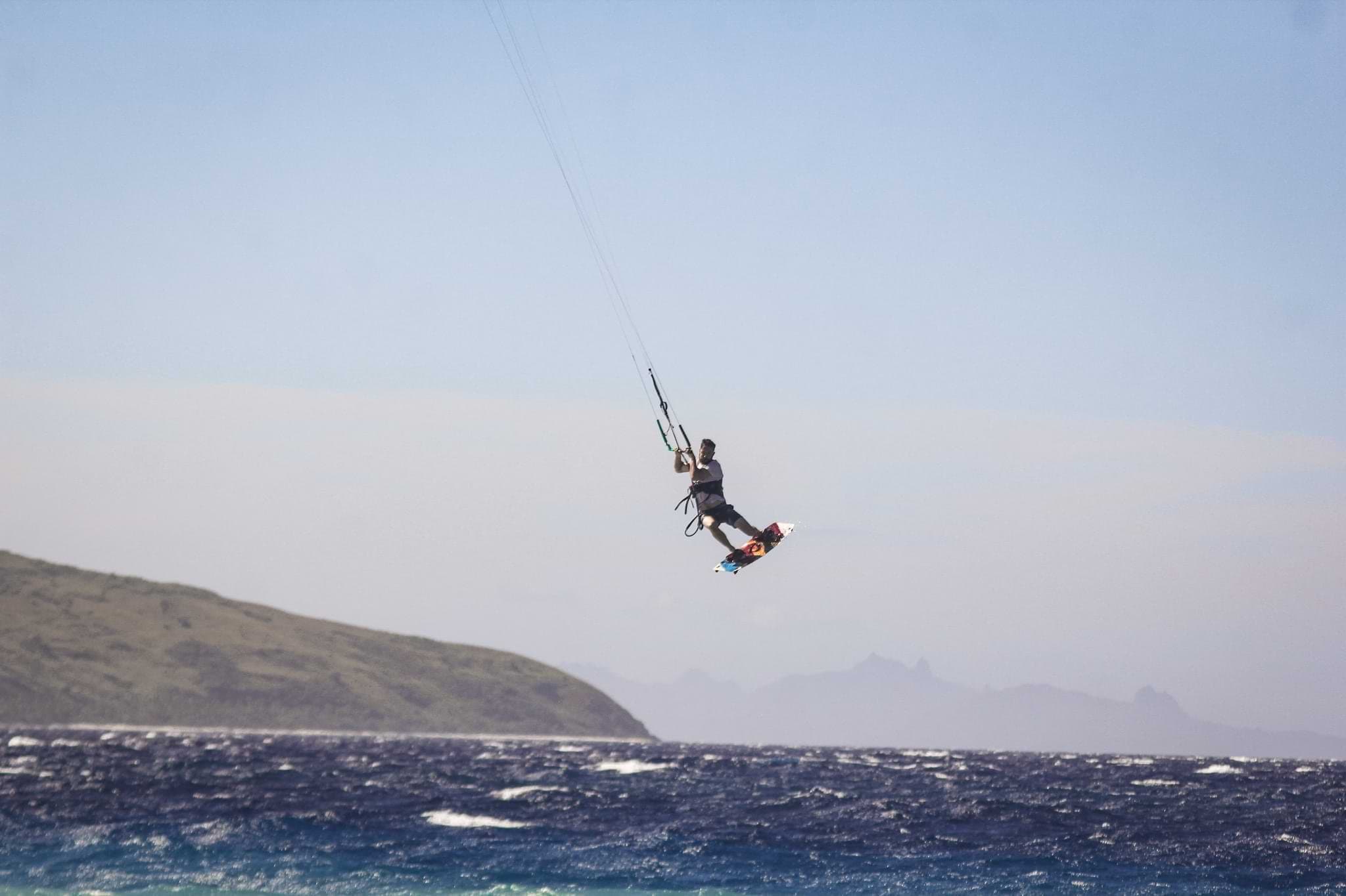 A kitesurfer jumping high above choppy water off Mana Island, Fiji.