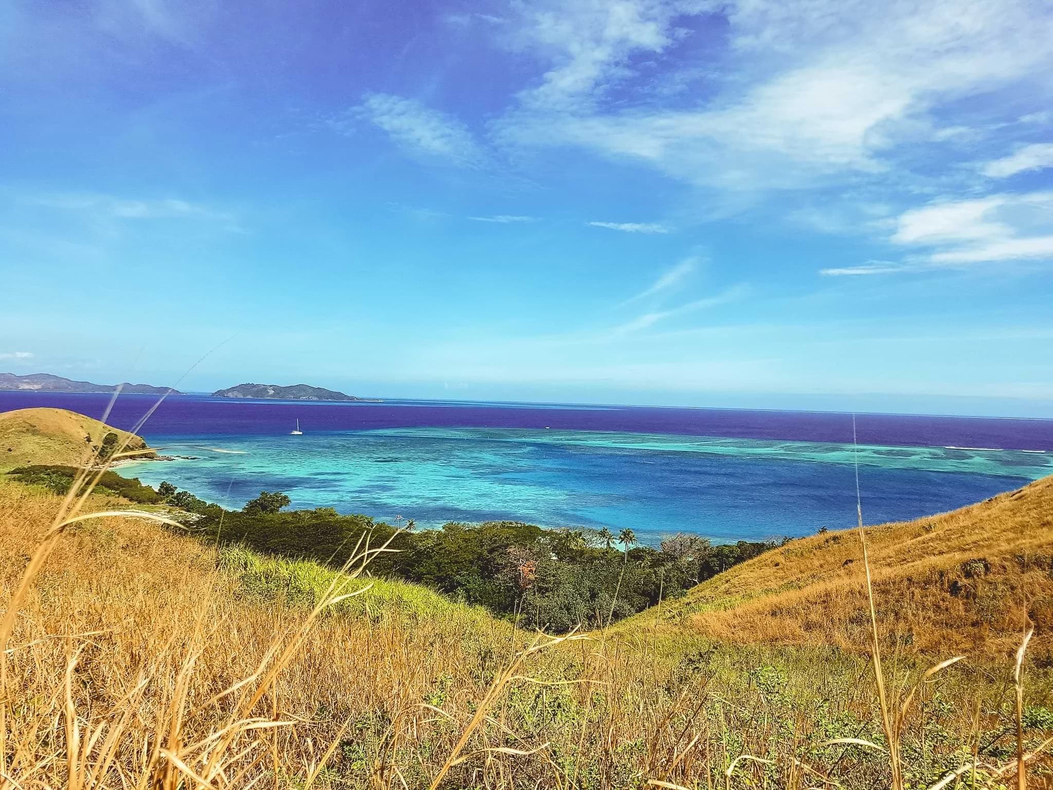 Turquoise reef shallows and deep-blue sea viewed from a grassy hillside on Mana Island.