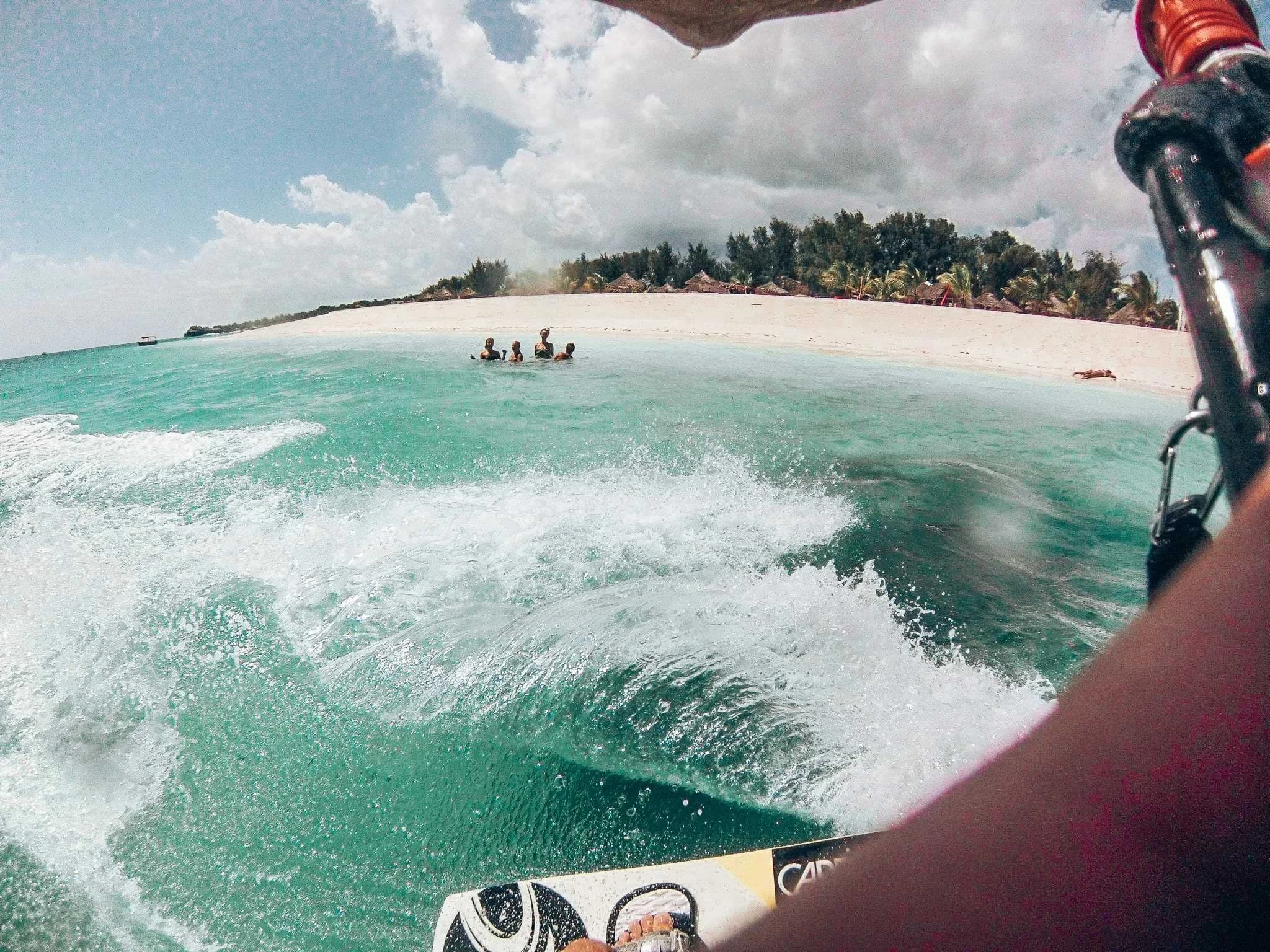 A kitesurfer’s view of spray and shallow turquoise water beside a palm-lined beach in Zanzibar.