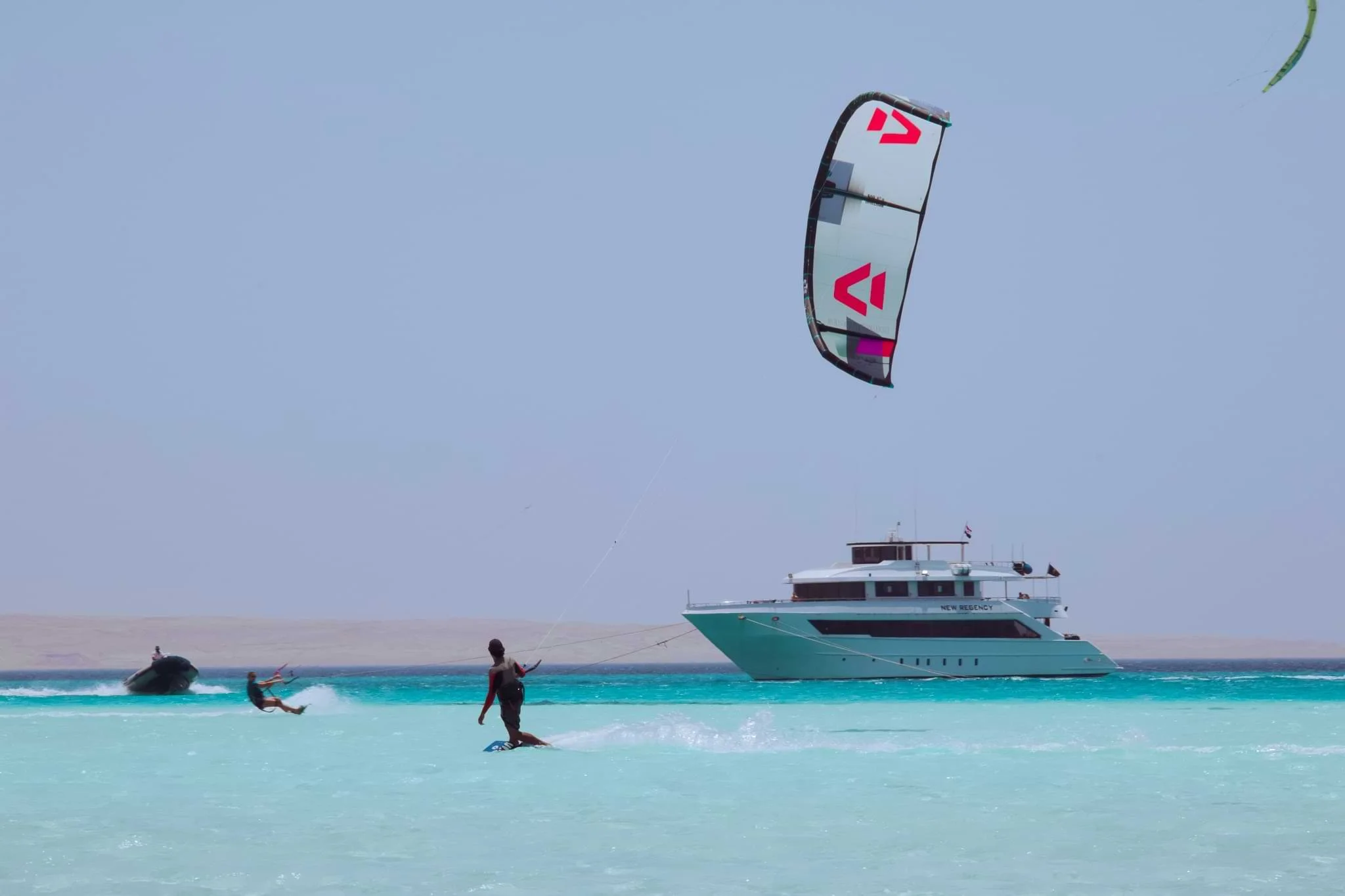 A kitesurfer riding through shallow turquoise water beside an anchored safari boat in Egypt.