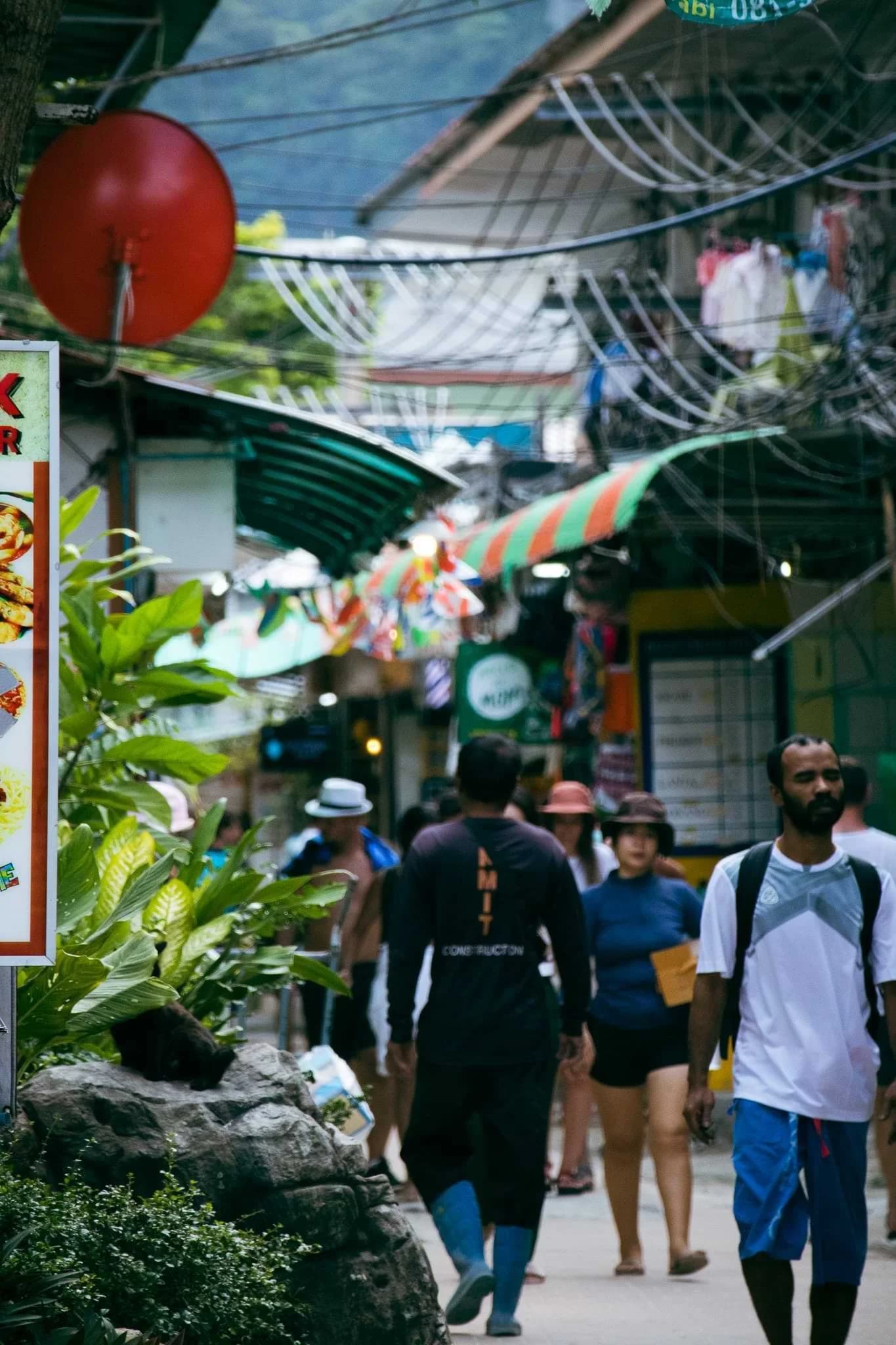 Pedestrians walking along a narrow shopping lane decorated with flags and lanterns.