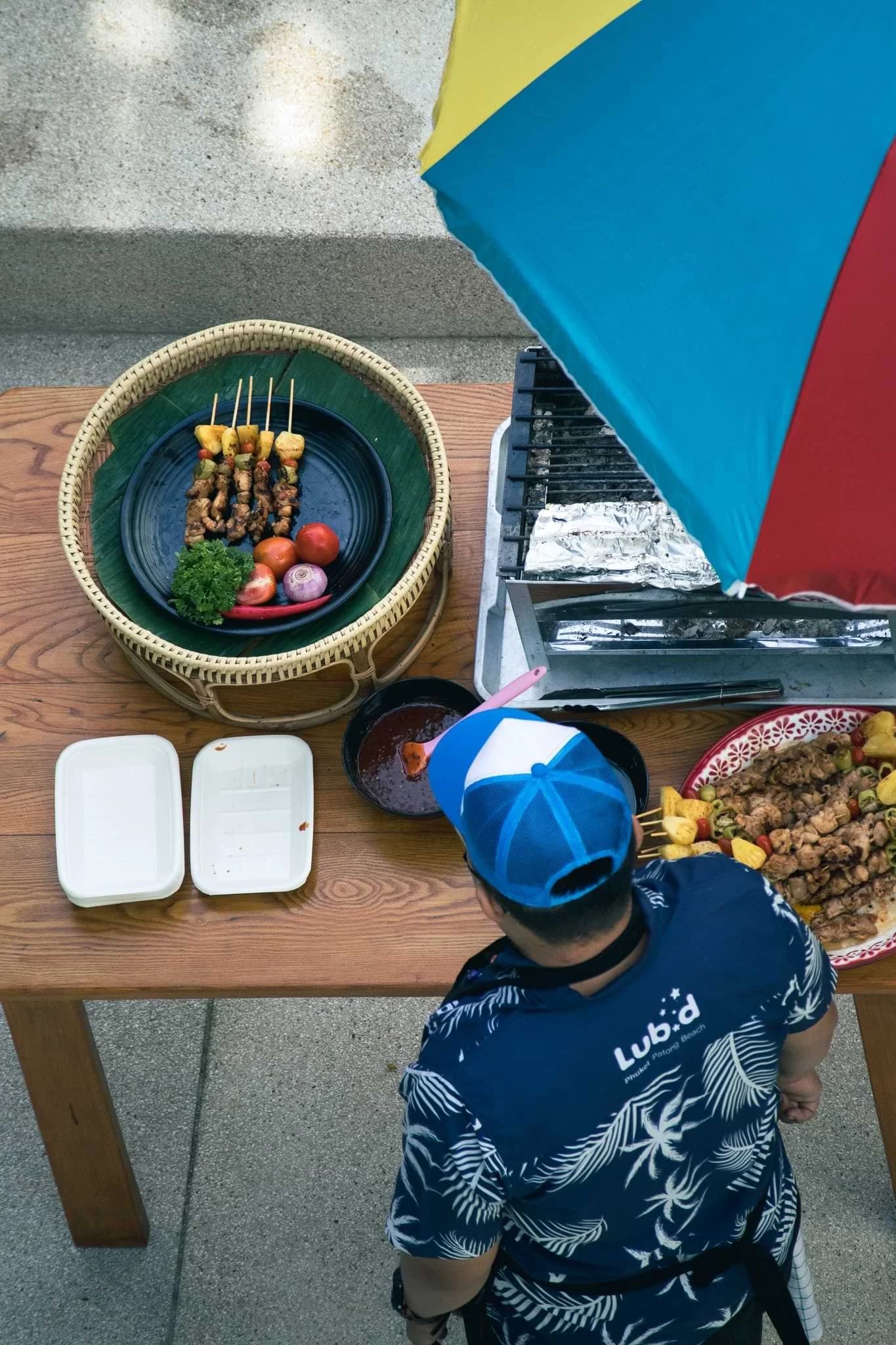 A staff member in a Lub d shirt serving food beneath a colourful umbrella, viewed from above.