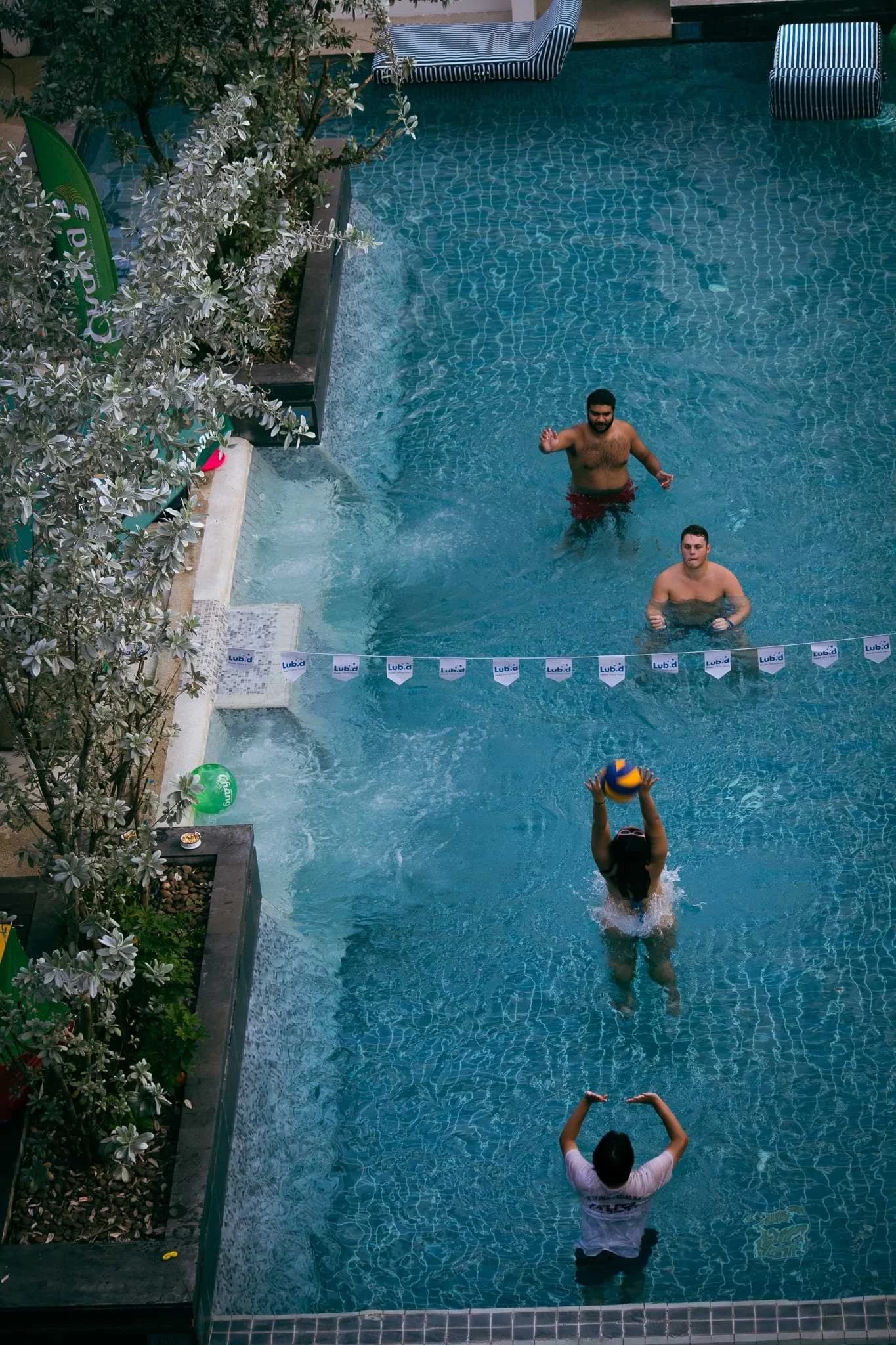Four people playing with a ball across a net in the swimming pool at Lub d Patong, viewed from above.