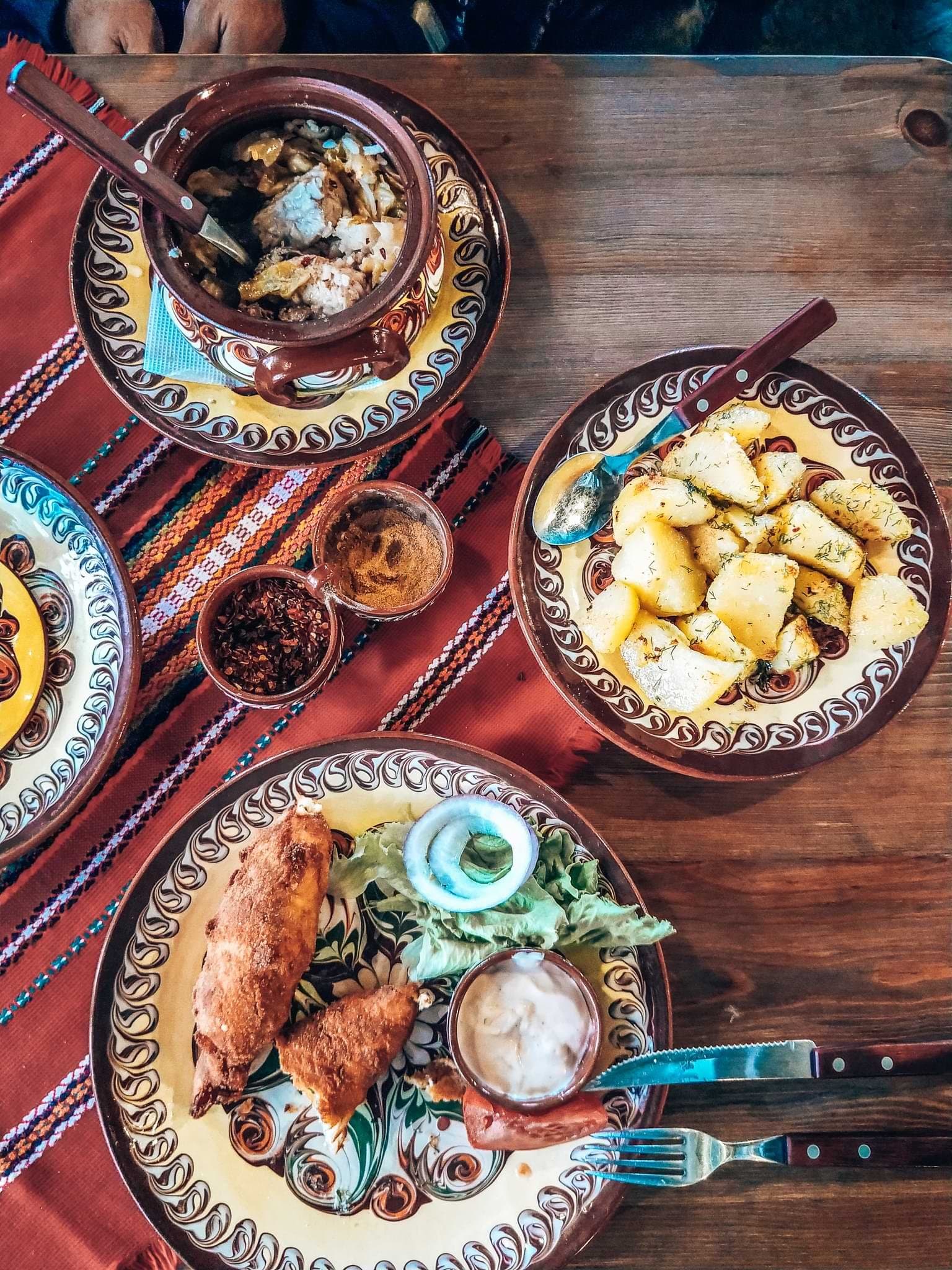 Traditional Bulgarian dishes in patterned ceramics, including potatoes, salad and breaded food.