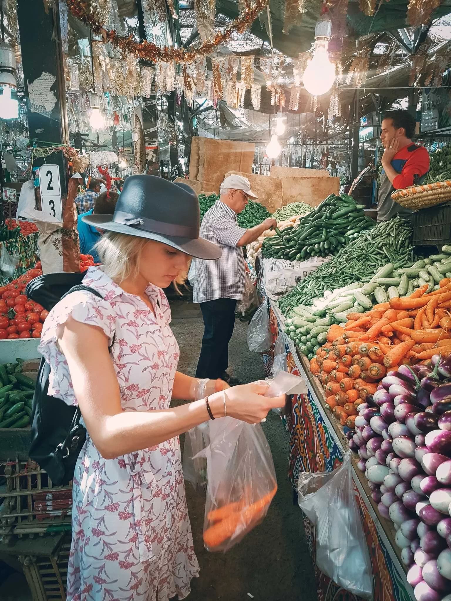 A shopper holding a bag beside stalls piled with vegetables at a market in Hurghada.